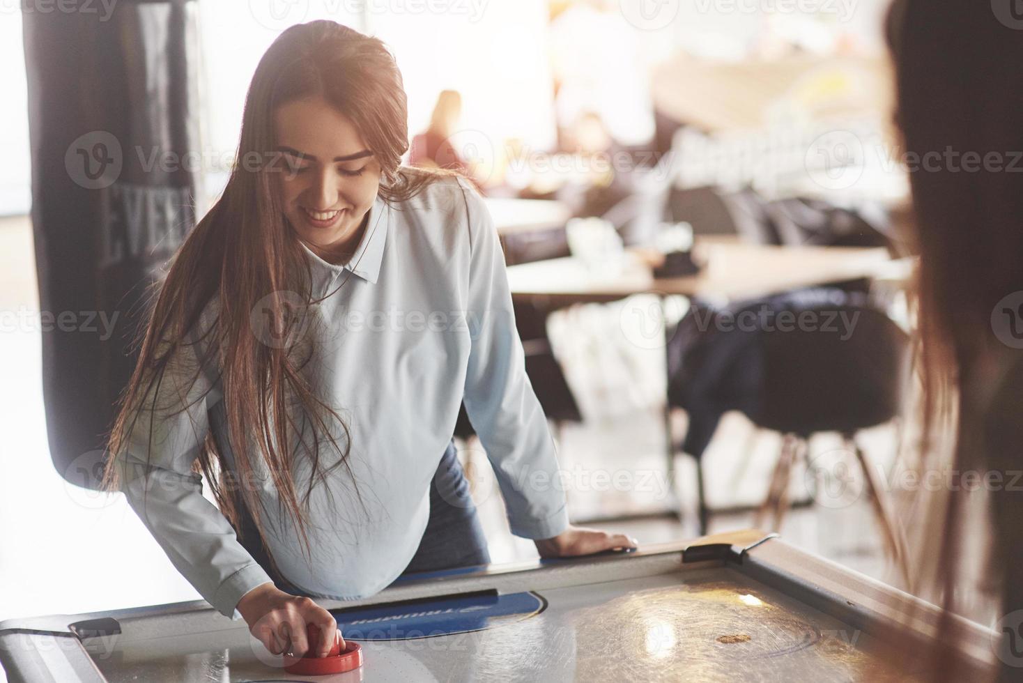 dos hermosas niñas gemelas juegan air hockey en la sala de juegos y se divierten foto