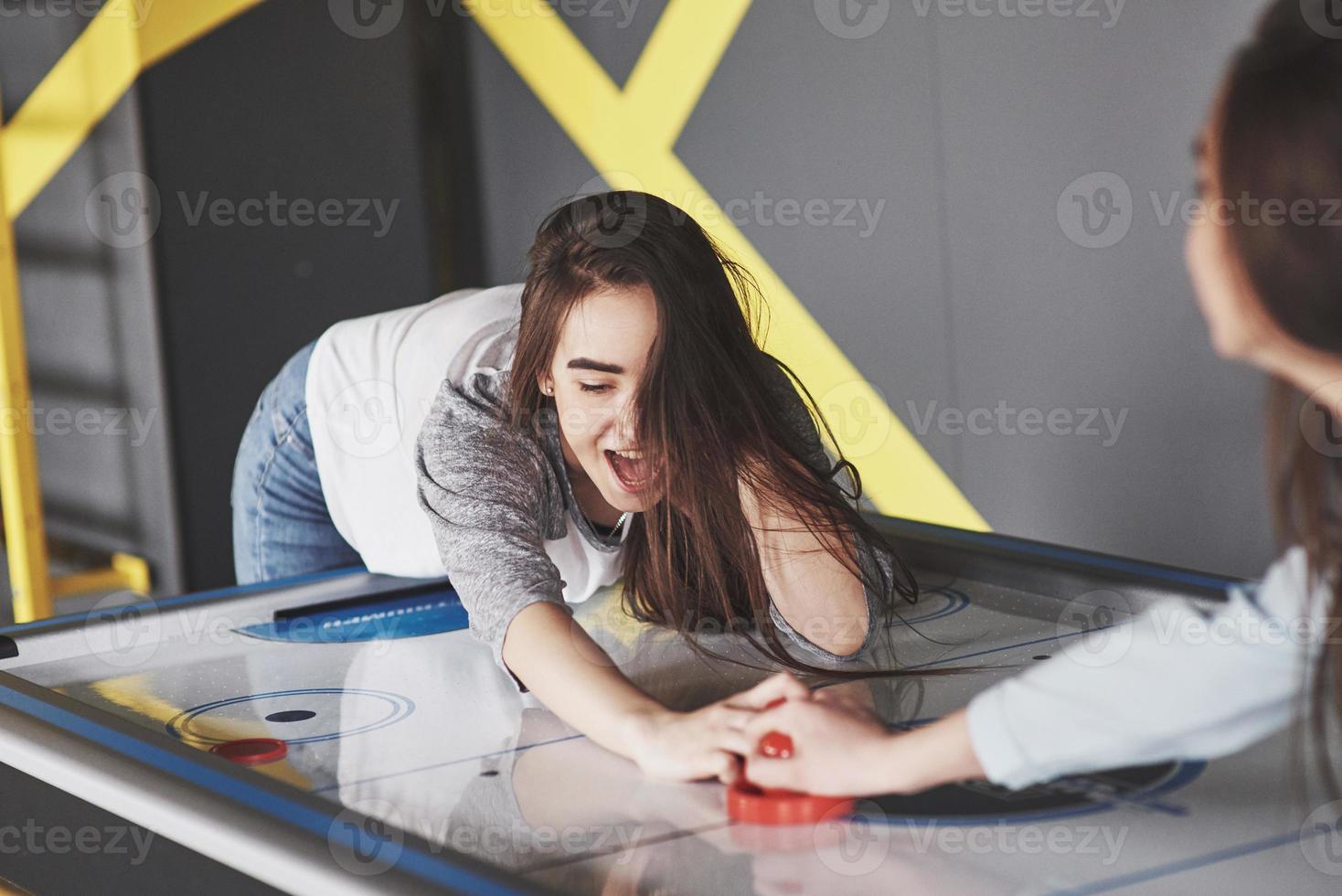 dos hermosas niñas gemelas juegan air hockey en la sala de juegos y se divierten foto