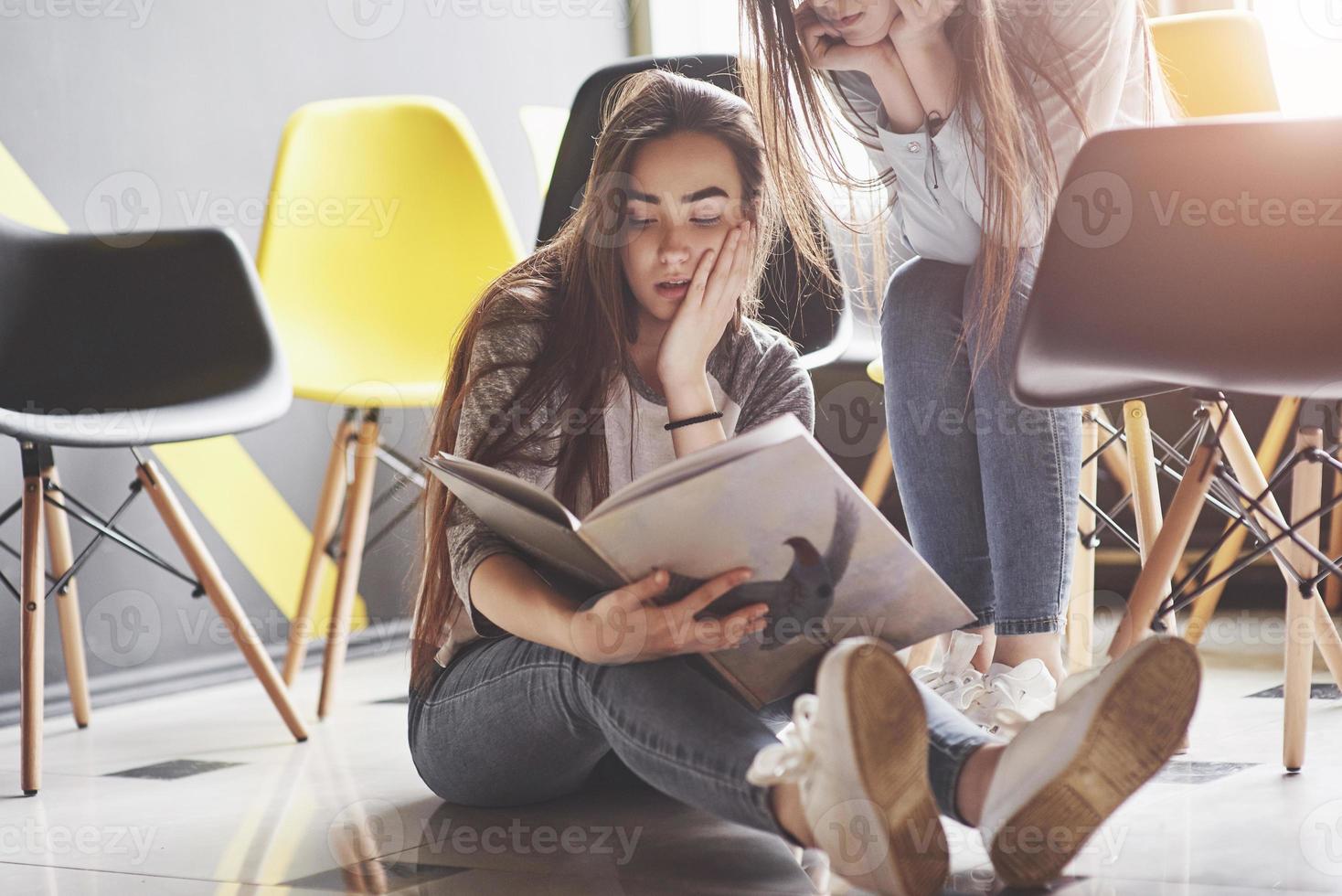 Two beautiful twin girls spend time read a book in library in the morning. Sisters relaxing in a cafe and having fun together photo