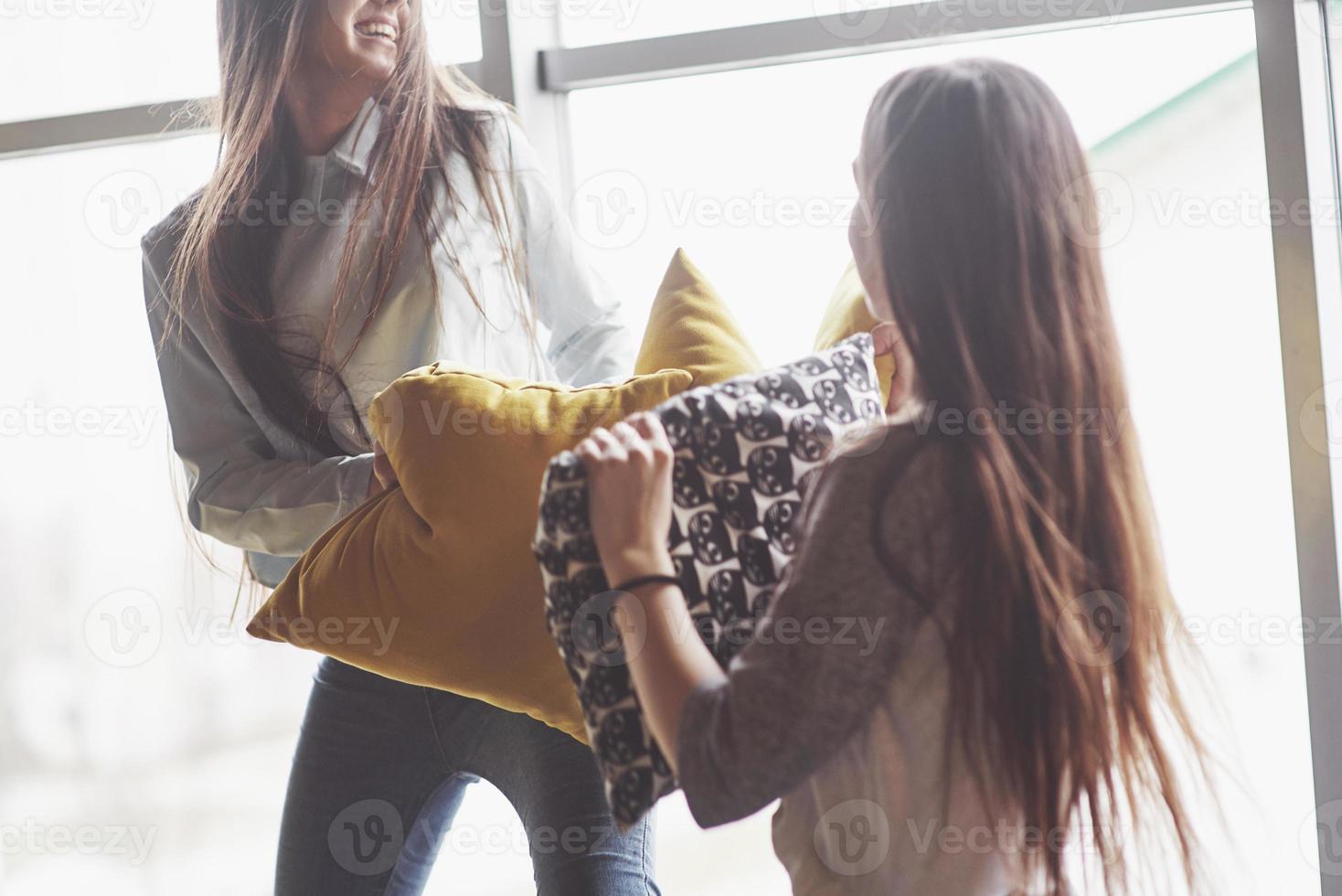 Two beautiful young twins sisters spending time together and are battling with pillows. Siblings having fun at home concept photo