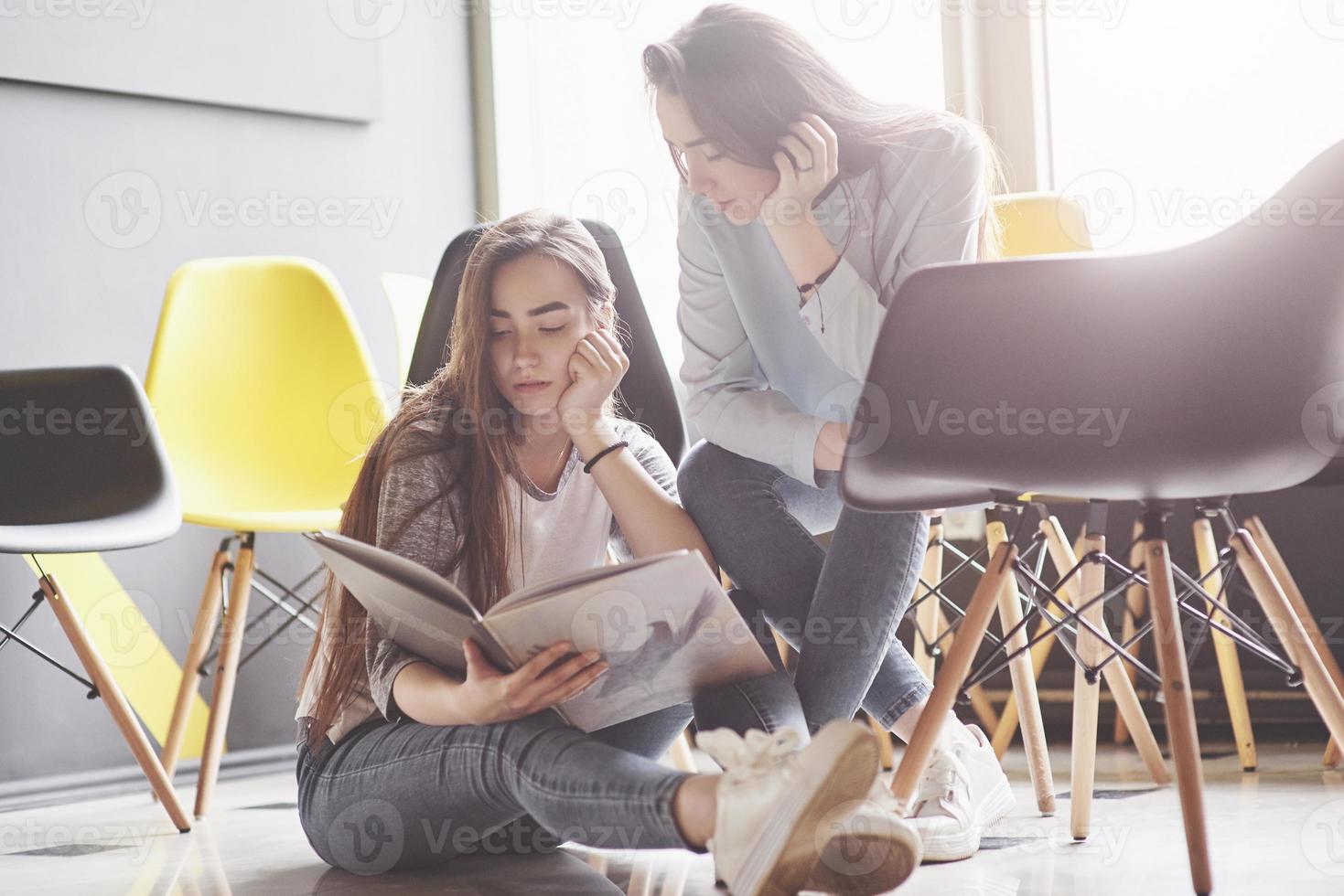 Two beautiful twin girls spend time read a book in library in the morning. Sisters relaxing in a cafe and having fun together photo