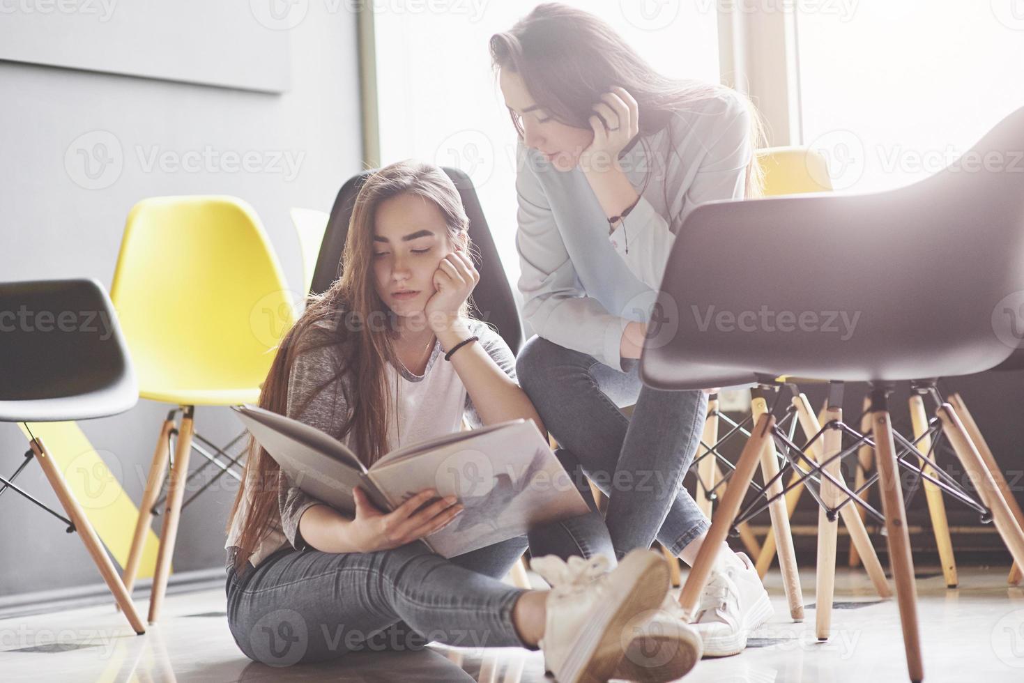 dos hermosas niñas gemelas pasan tiempo leyendo un libro en la biblioteca por la mañana. hermanas relajándose en un café y divirtiéndose juntas foto