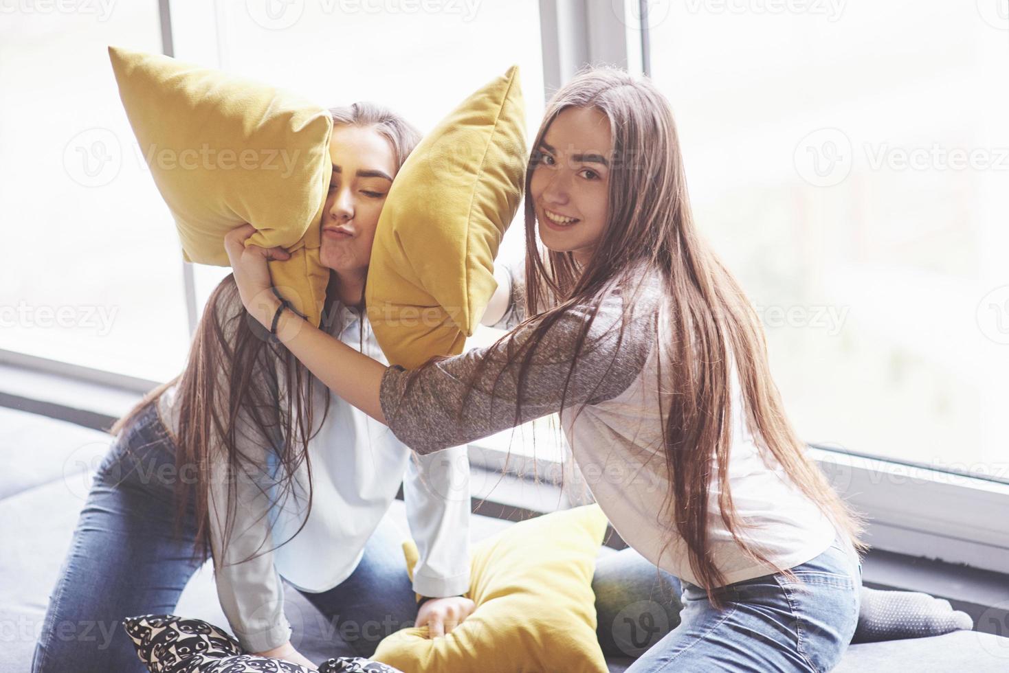 Two beautiful young twins sisters spending time together with pillows. Siblings having fun at home concept photo