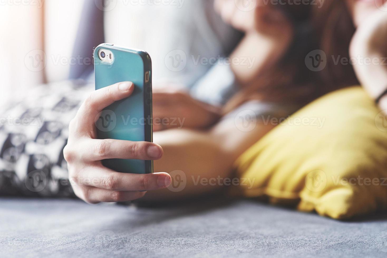 dos lindas hermanas gemelas sonrientes sosteniendo smartphone y haciendo selfie. las niñas se acuestan en el sofá posando y alegría foto