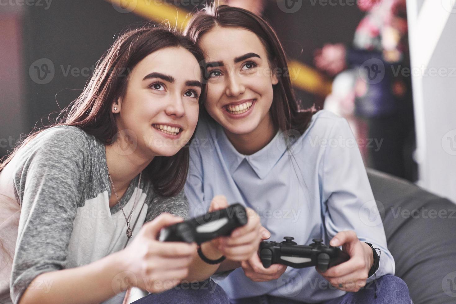 Twin sister sisters play on the console. Girls hold joysticks in their hands and have fun photo