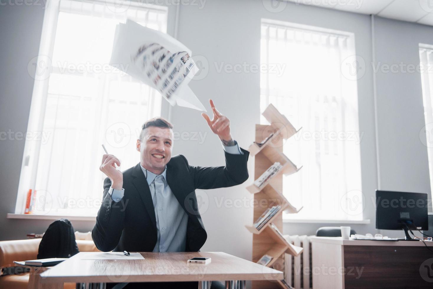 un hombre guapo sentado en la oficina y tirando papeles al aire foto