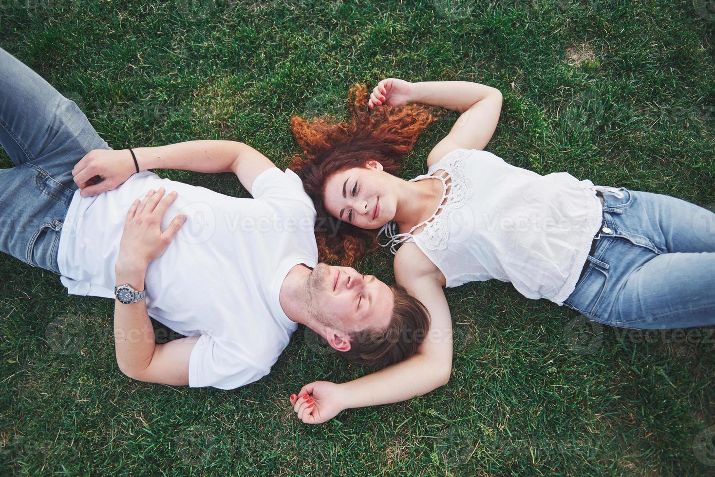 Romantic couple of young people lying on grass in park. They look happy. View from above. photo