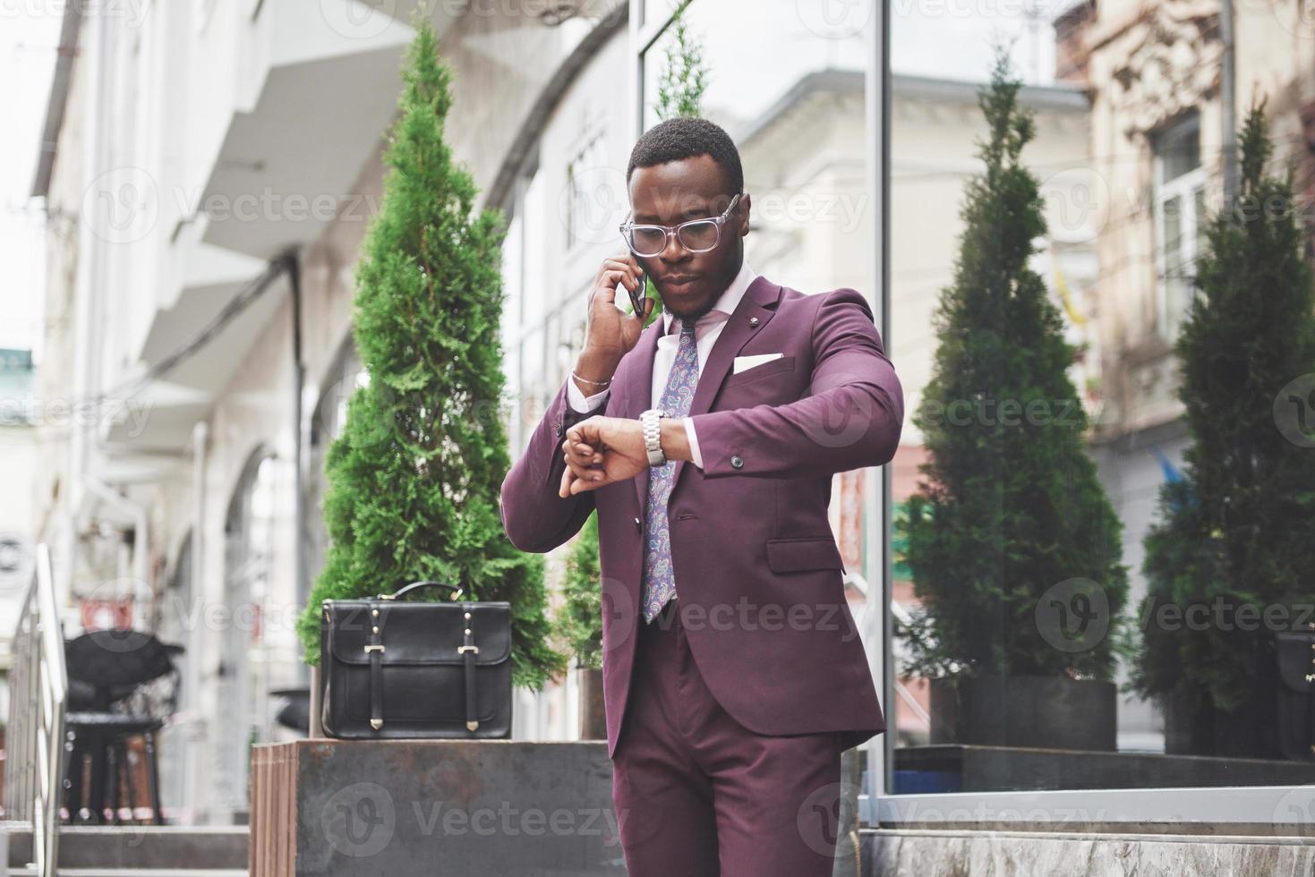 Portrait of a young and handsome African American businessman talking in a suit over the phone. Preparing for a business meeting. photo