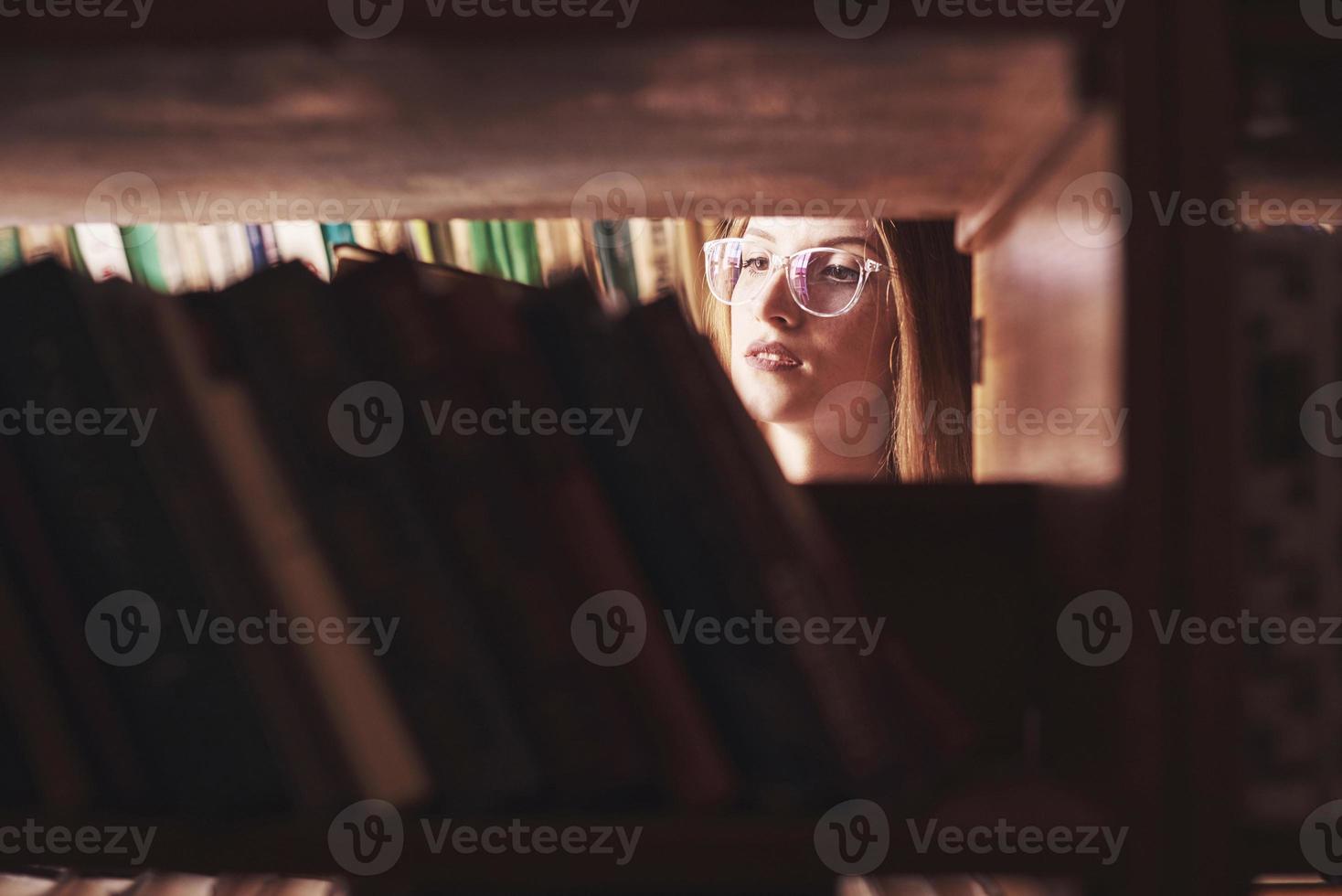 A young student girl is looking for the right book on the shelves of the old university library photo