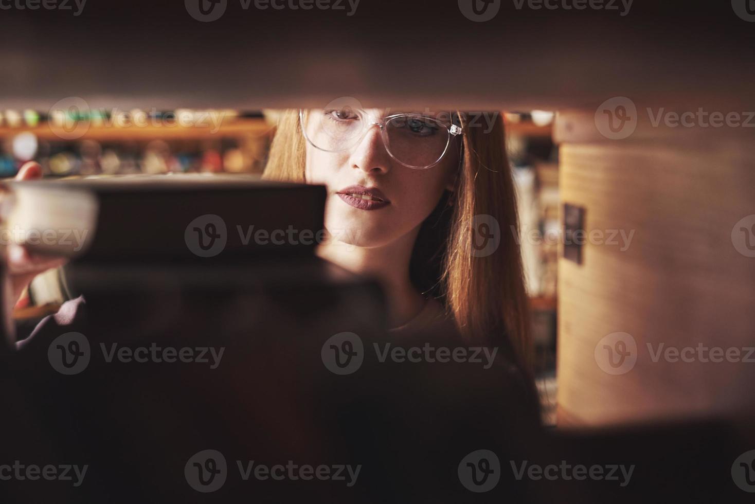 A young student girl is looking for the right book on the shelves of the old university library photo