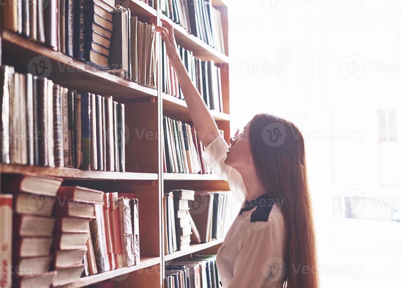 A young student girl is looking for the right book on the shelves of the old university library photo