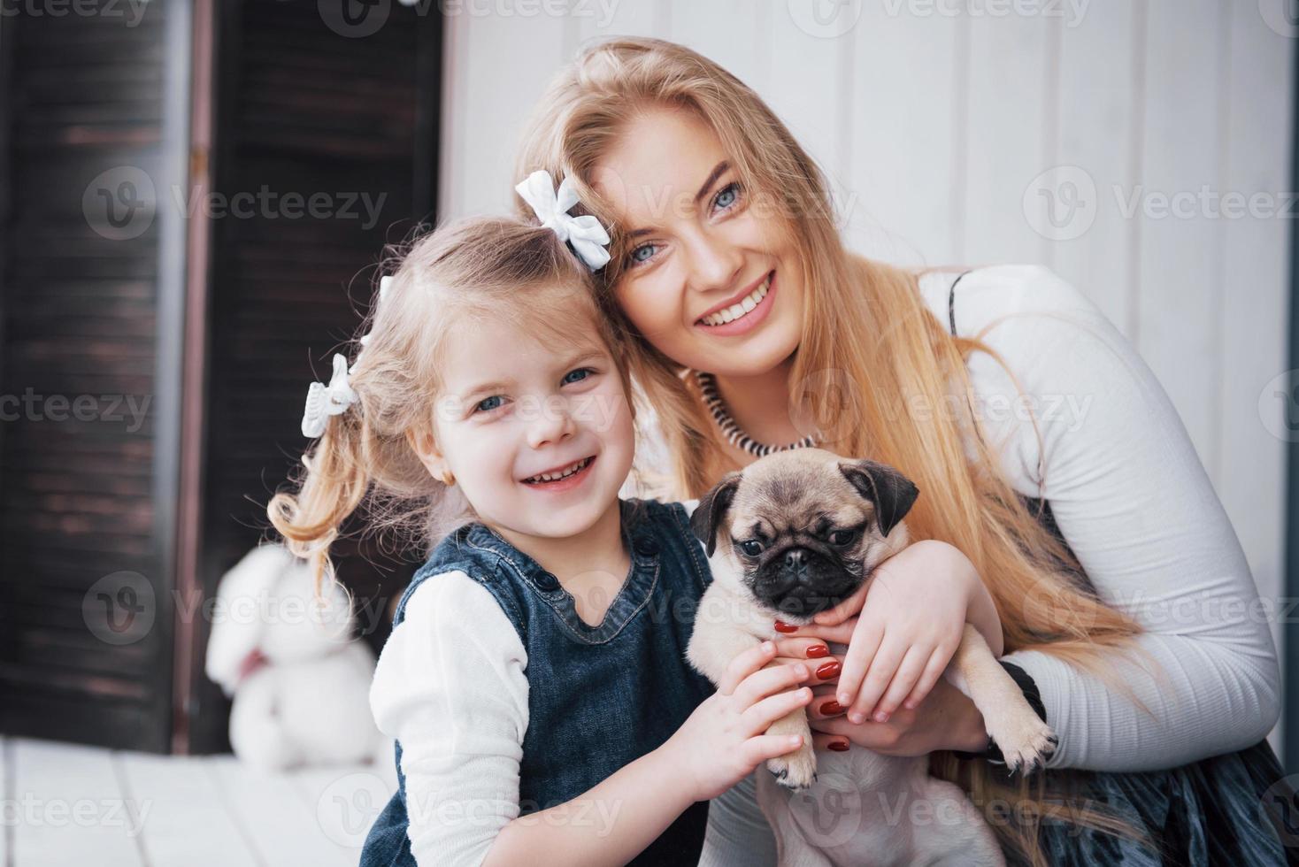 familia amorosa feliz. madre y su hija niña jugando y abrazando adorable pug foto