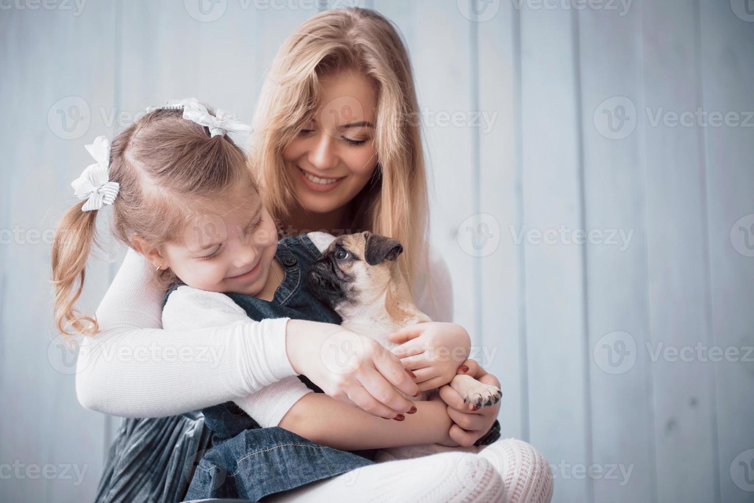 familia amorosa feliz. madre y su hija niña jugando y abrazando adorable pug foto