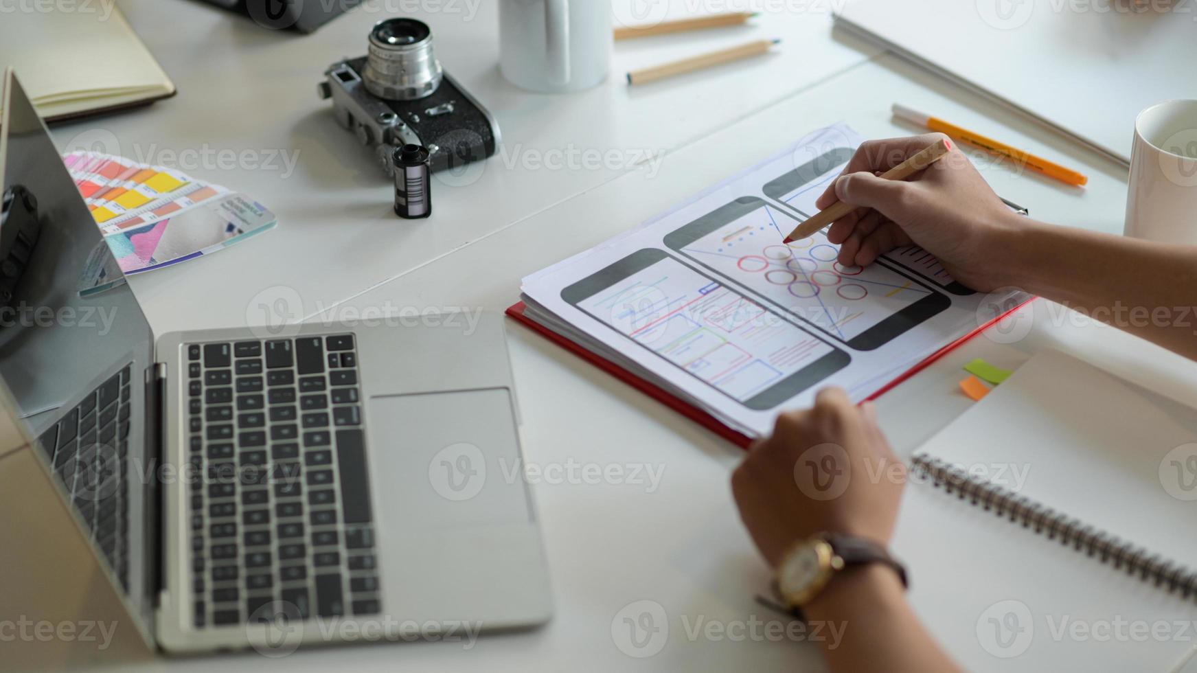 El diseñador está dibujando una pantalla de teléfono inteligente para futuros clientes en el escritorio con computadora portátil y artículos de papelería. foto