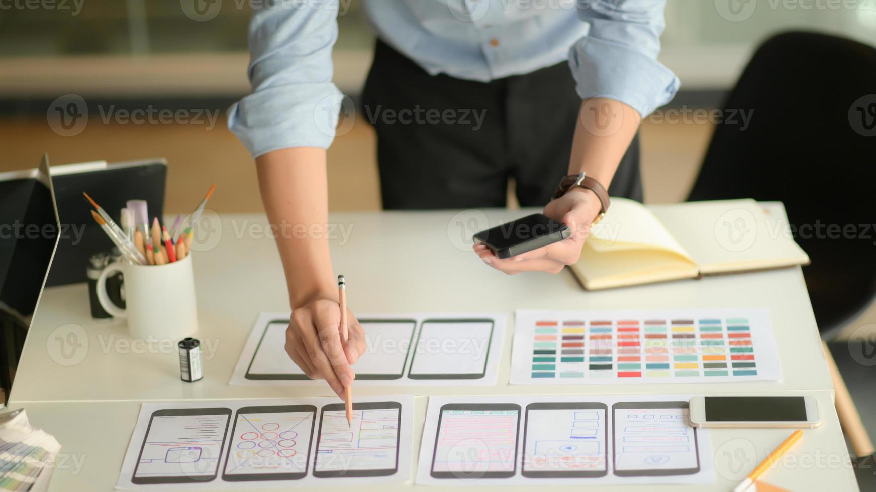 Cropped shot of young ux designer working on new application project while using smartphone in modern office room. photo