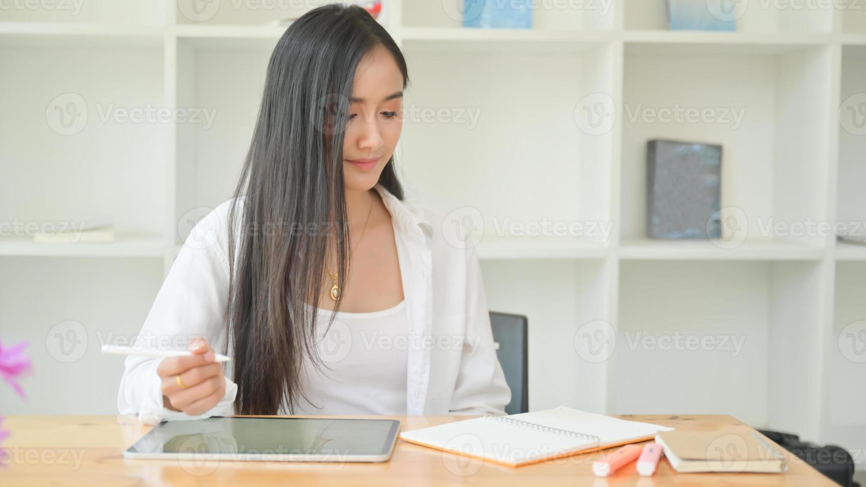 una joven diseñadora que sostiene un bolígrafo en la mano está usando una tableta para diseñar su nuevo proyecto. foto