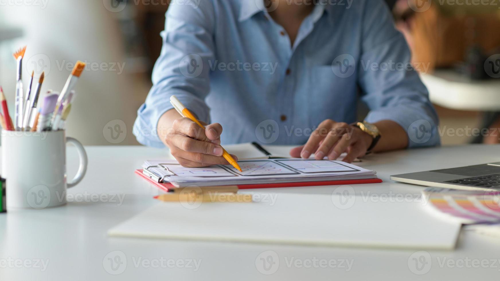 El diseñador está dibujando una pantalla de teléfono inteligente para futuros clientes en el escritorio con computadora portátil y artículos de papelería. foto