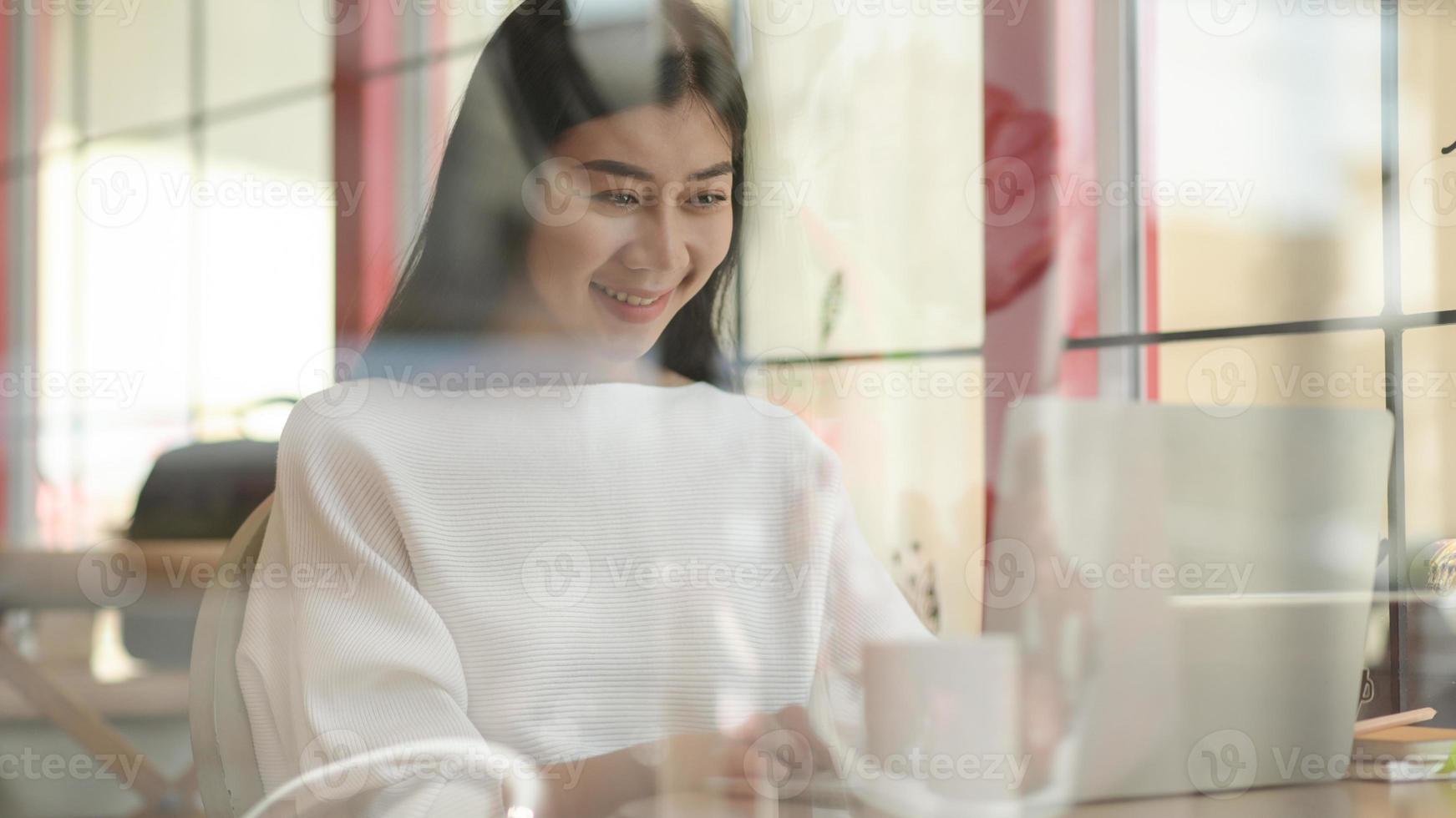 Young girl uses a laptop for video conference in a cafe, Shot from the outside through the glass. photo