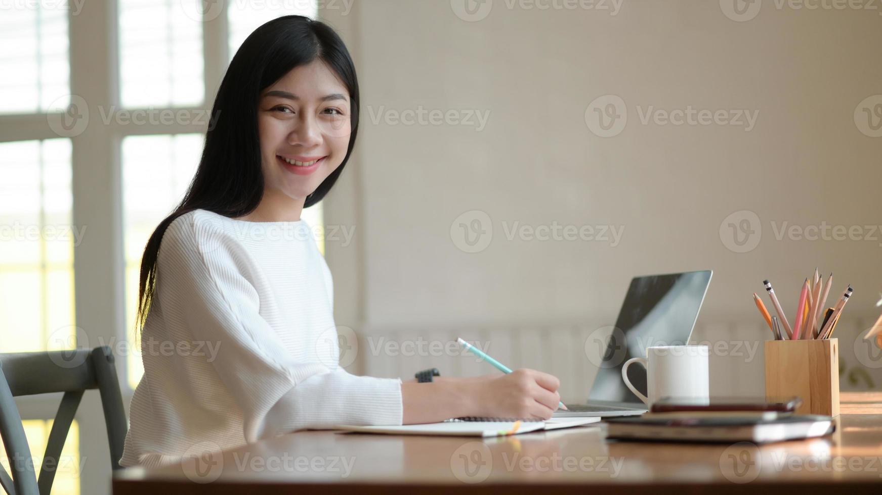 Young female student take notes and use laptop to search for research to prepare for graduation. photo