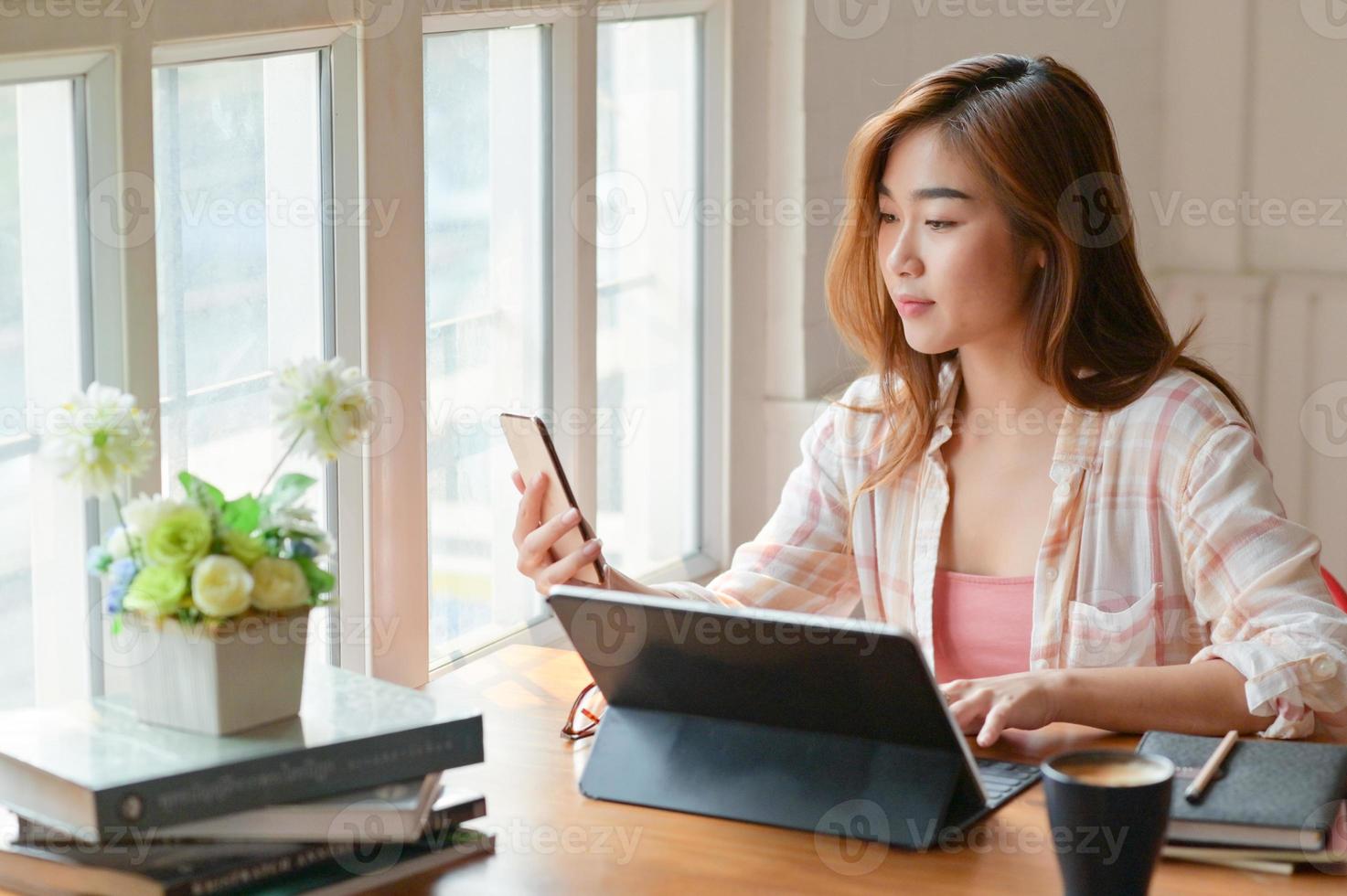 A portrait of a Asian female student is using a smartphone and a laptop to prepare for university graduation. photo