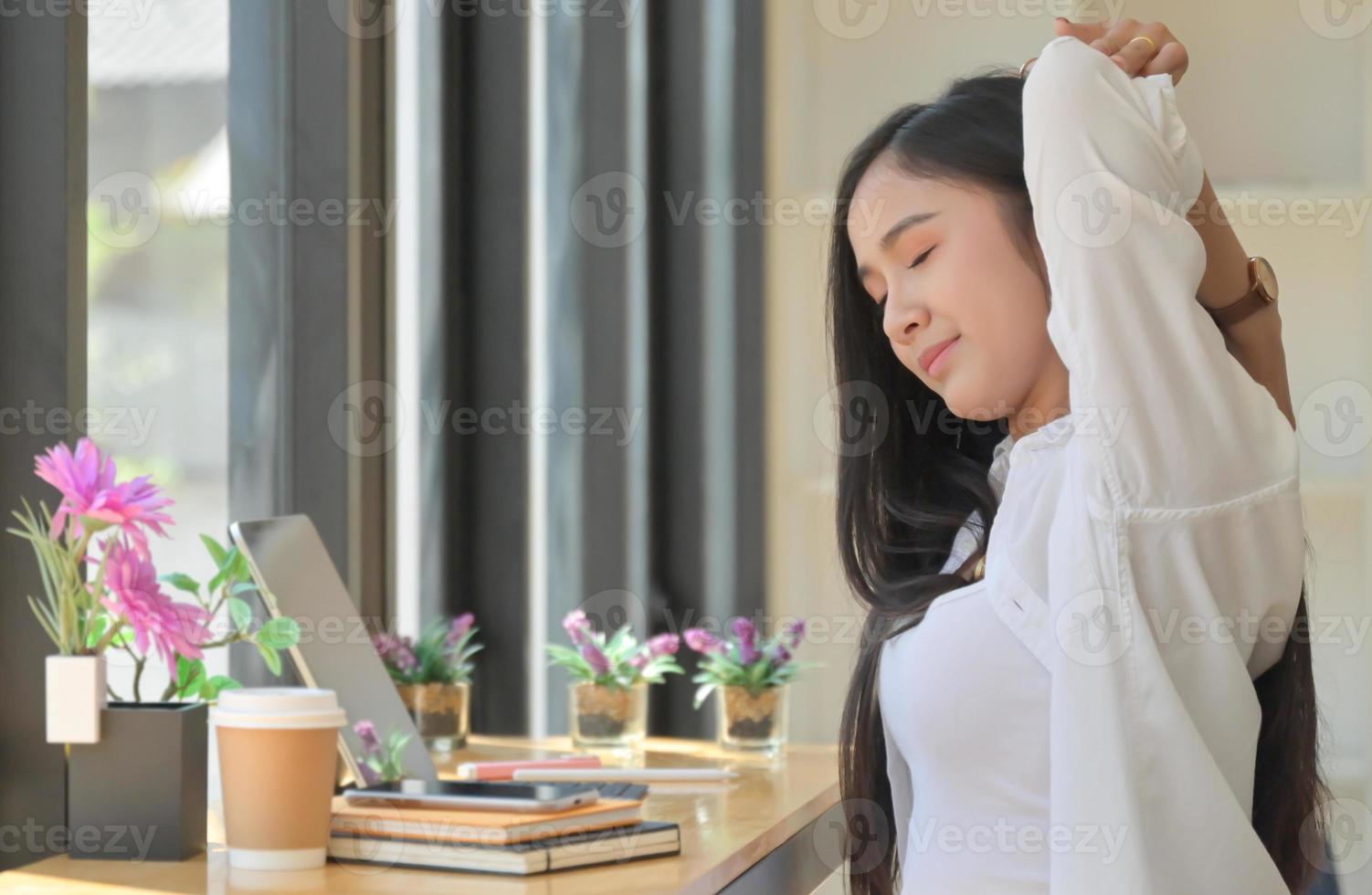 Asian women sit in the workspace and stretch their arms to relax during an online meeting with a laptop. photo