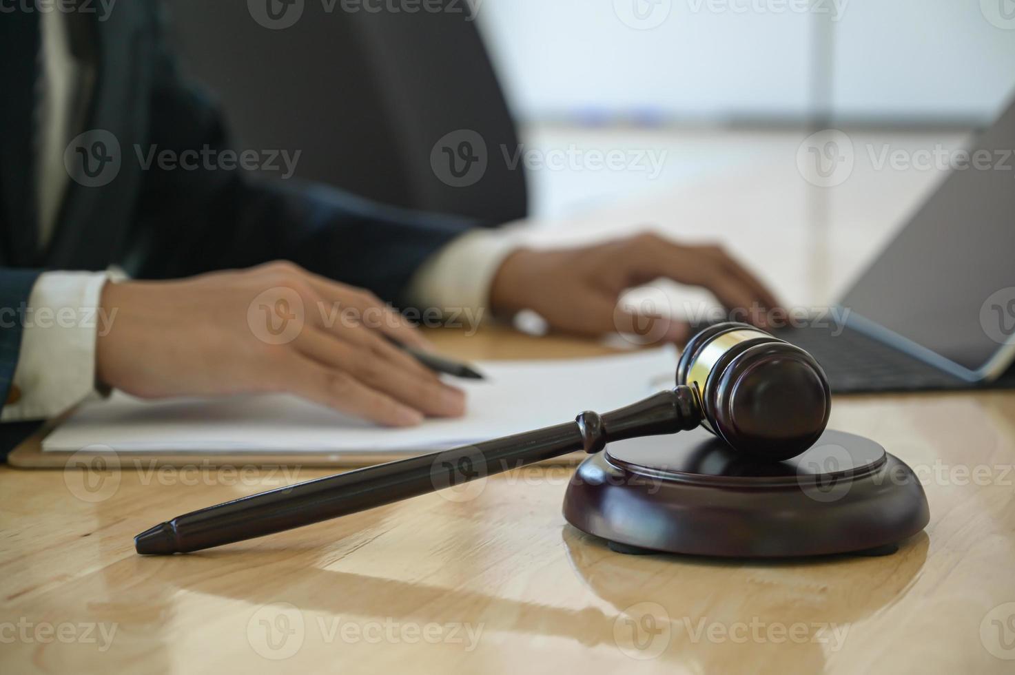 concepto de justicia, martillo colocado en la mesa de trabajo con un abogado utiliza una computadora portátil sentada detrás. foto