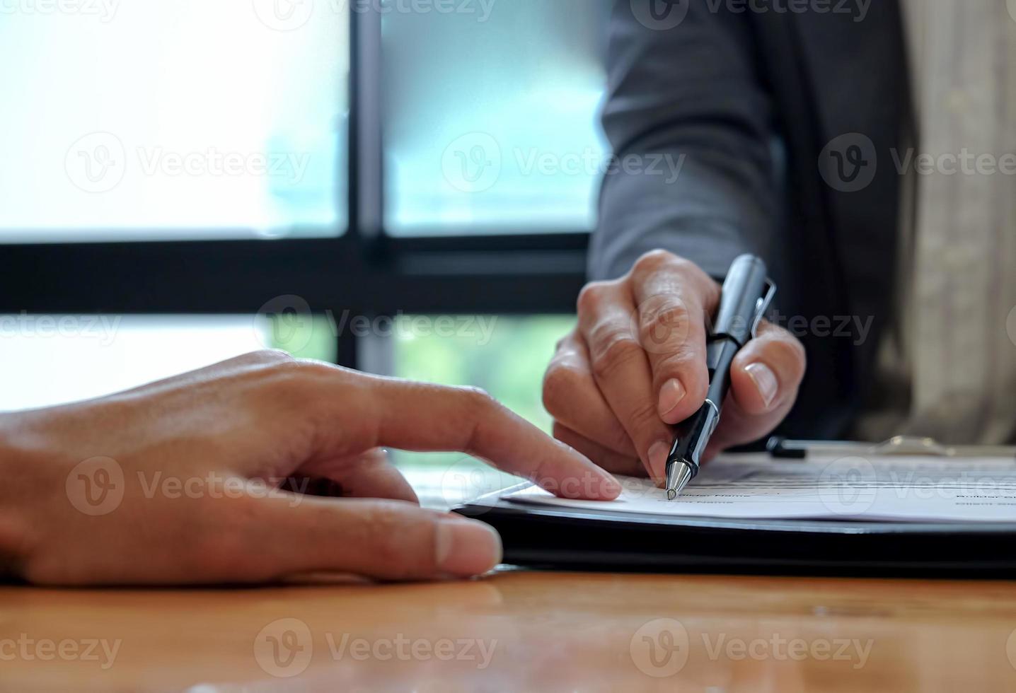 La mano del vendedor señala al cliente para que utilice el bolígrafo para firmar el contrato. foto