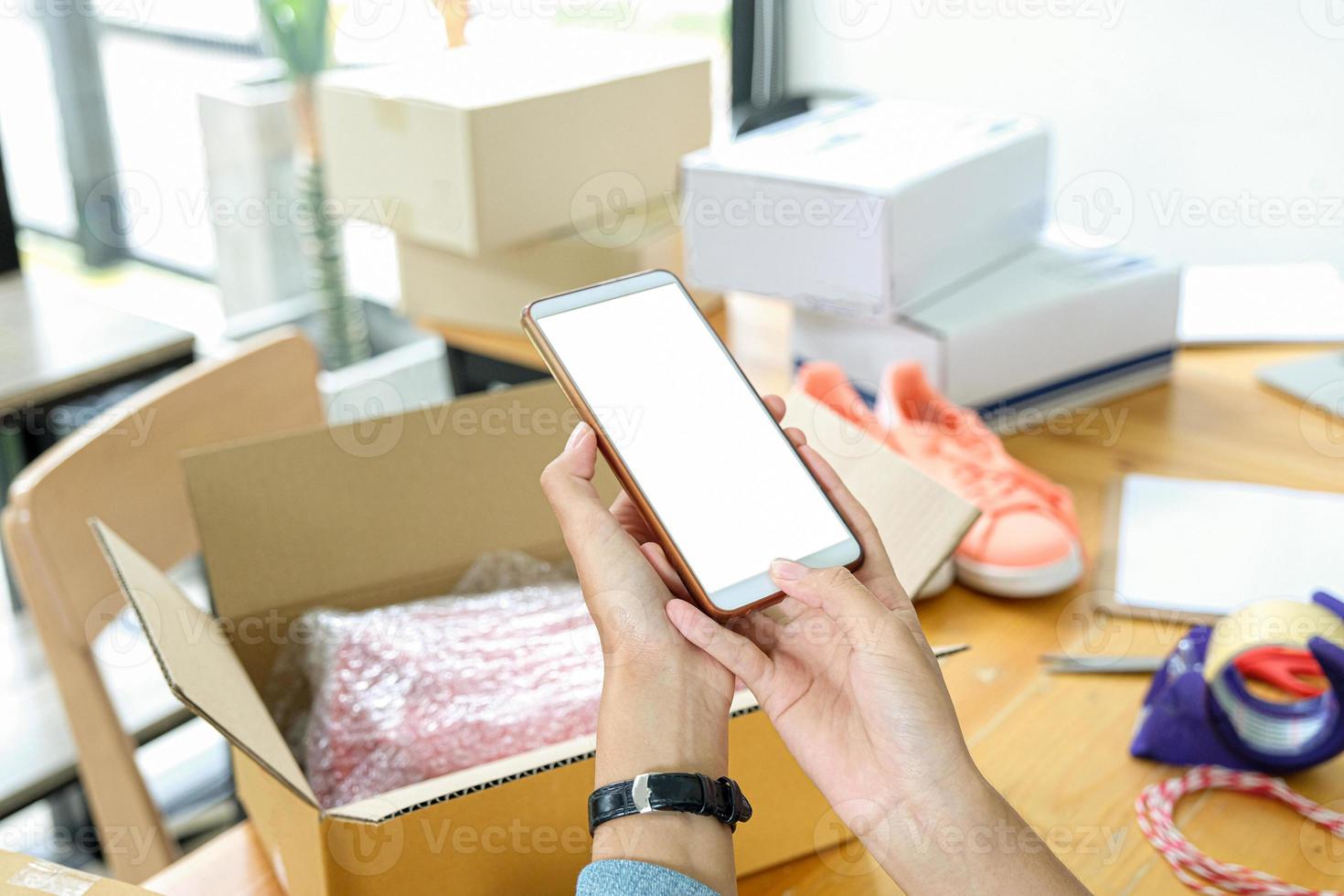 El vendedor en línea utiliza el teléfono móvil para tomar fotografías de los productos en la caja y enviarlos al cliente. foto