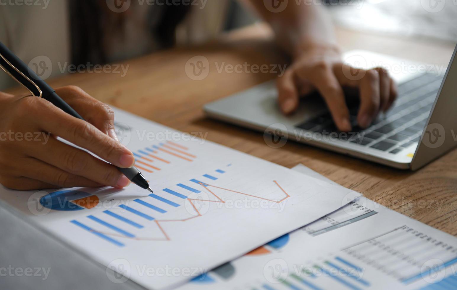 Female businessmen point the pen at the data graph and use the laptop to work. photo