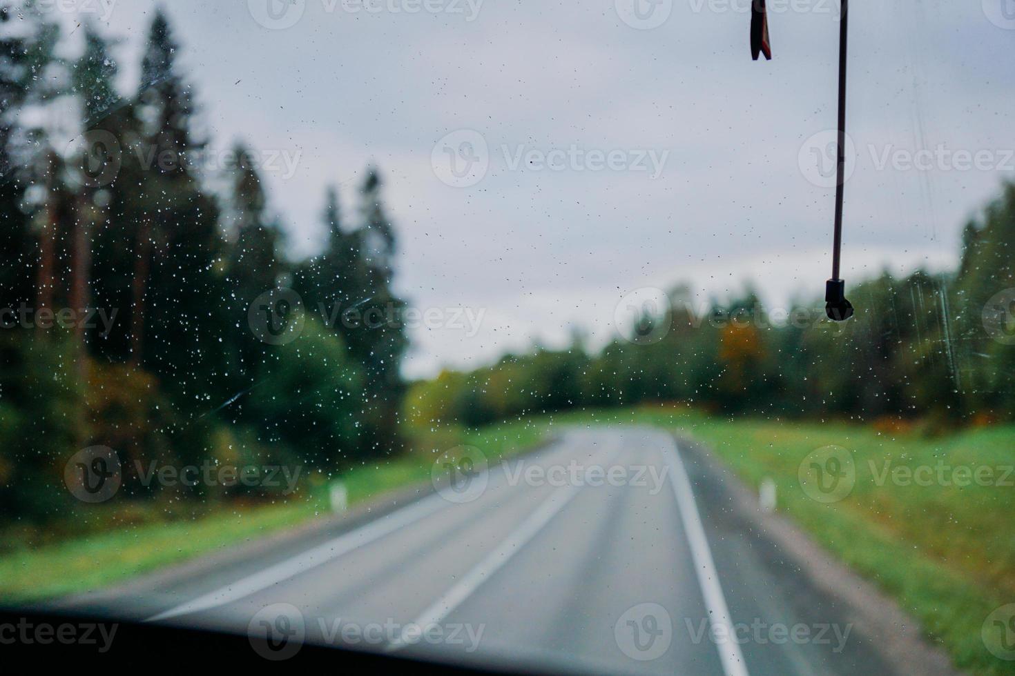 Rain water drop on the window. View of the road and the autumn forest photo