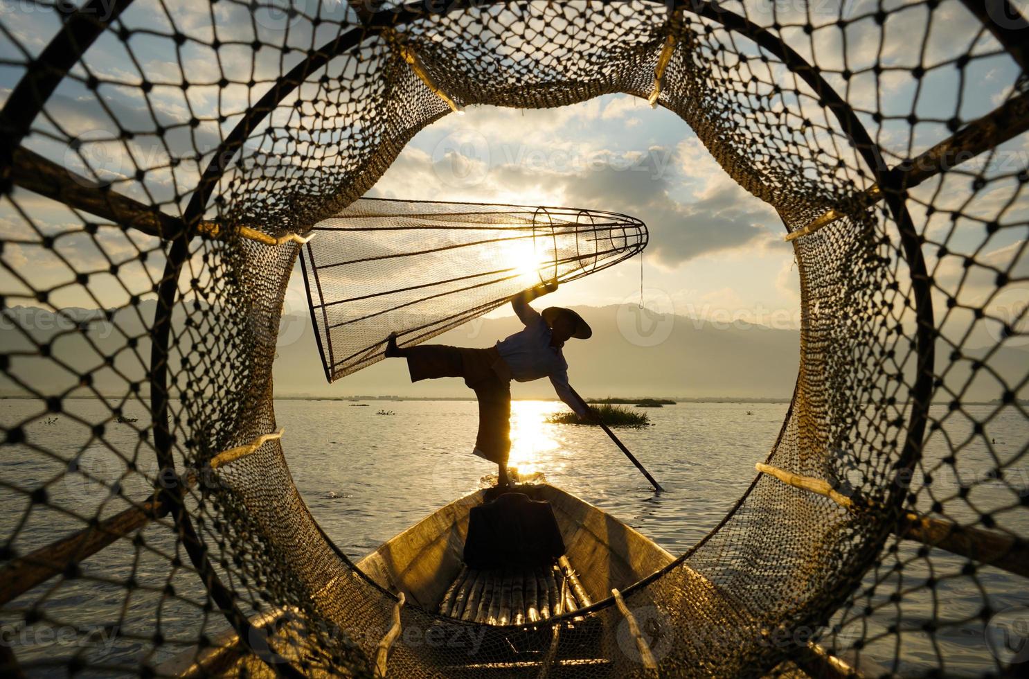 View through fish coop of local fisherman standing on boat in lake at sunrise photo