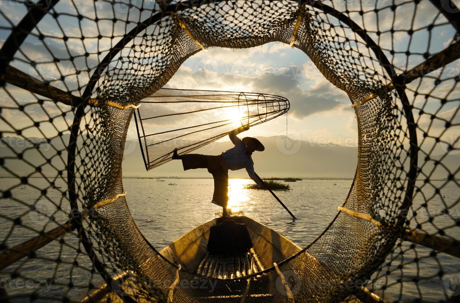 Ver a través del gallinero de los pescadores locales de pie en el barco en el lago al amanecer. foto