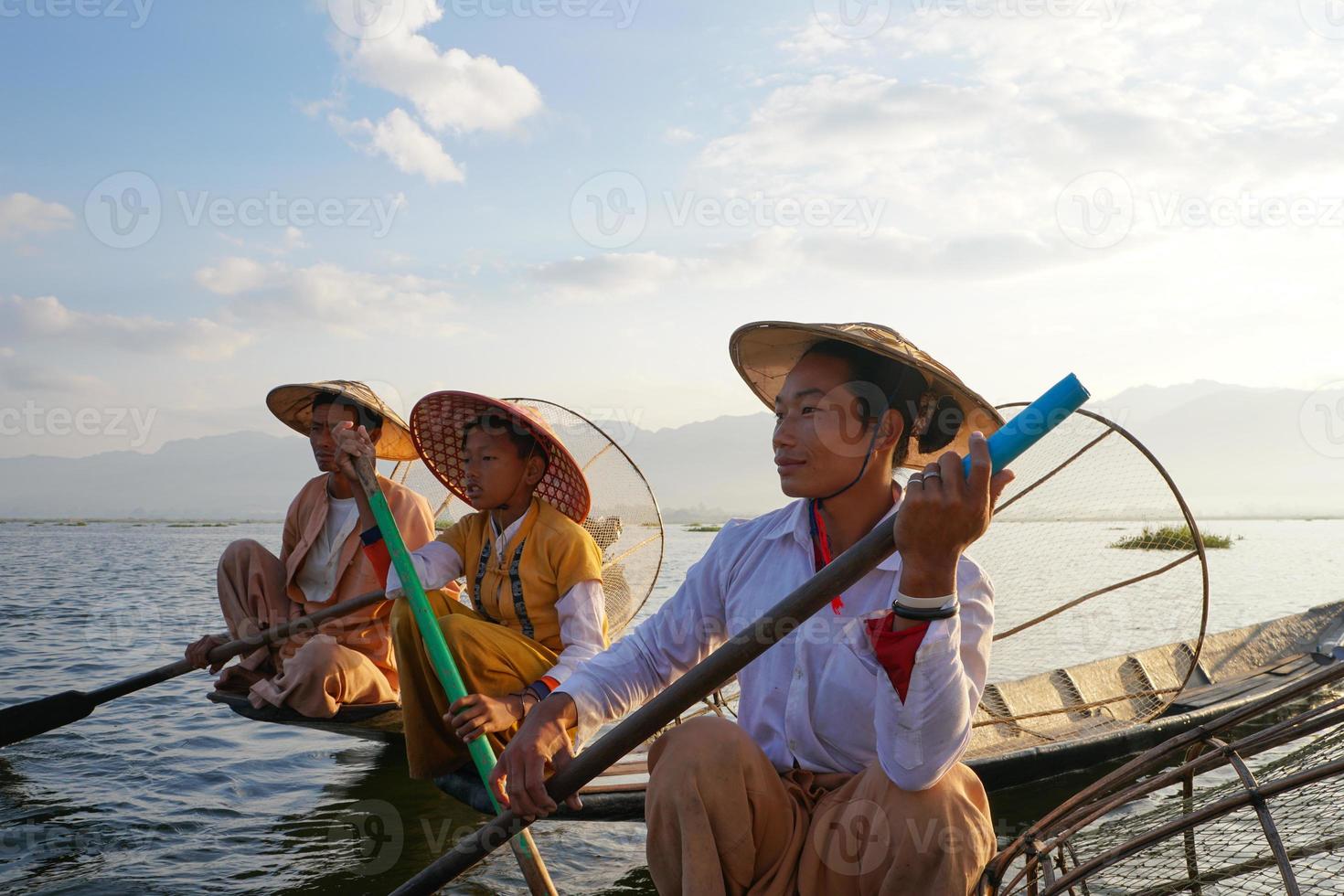 Familia de pescadores asiáticos locales, incluidos padre e hijos en barco en el lago Inle foto