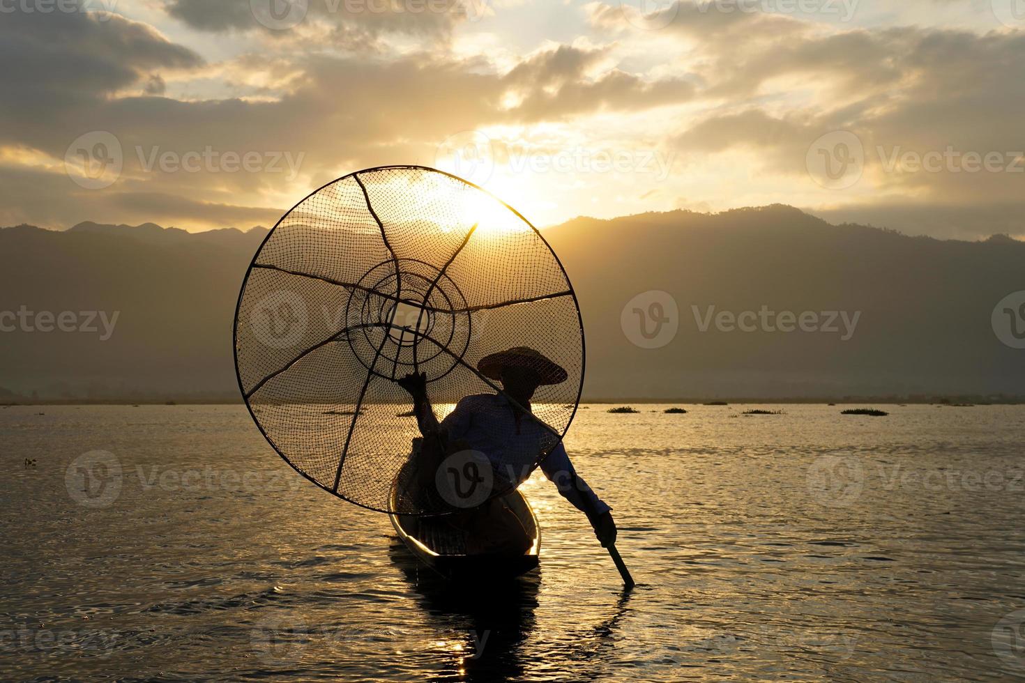 Silueta de pescador local usando coop para pescar en el lago Inle al amanecer. foto