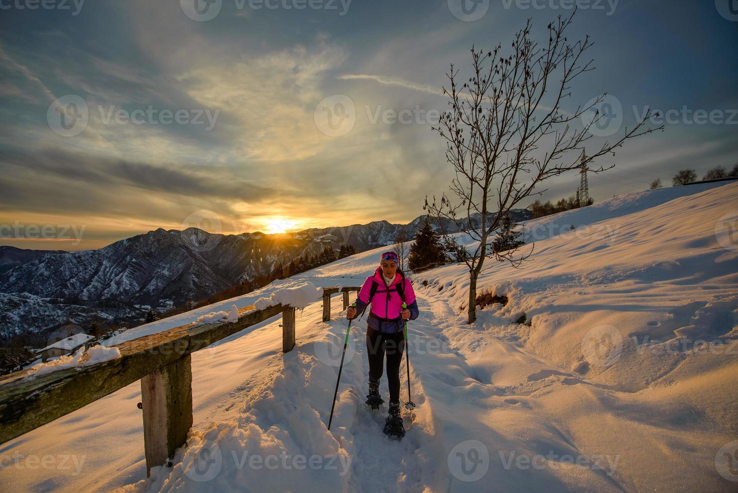 Mujer joven sola en caminata con raquetas de nieve en el hermoso día del atardecer foto