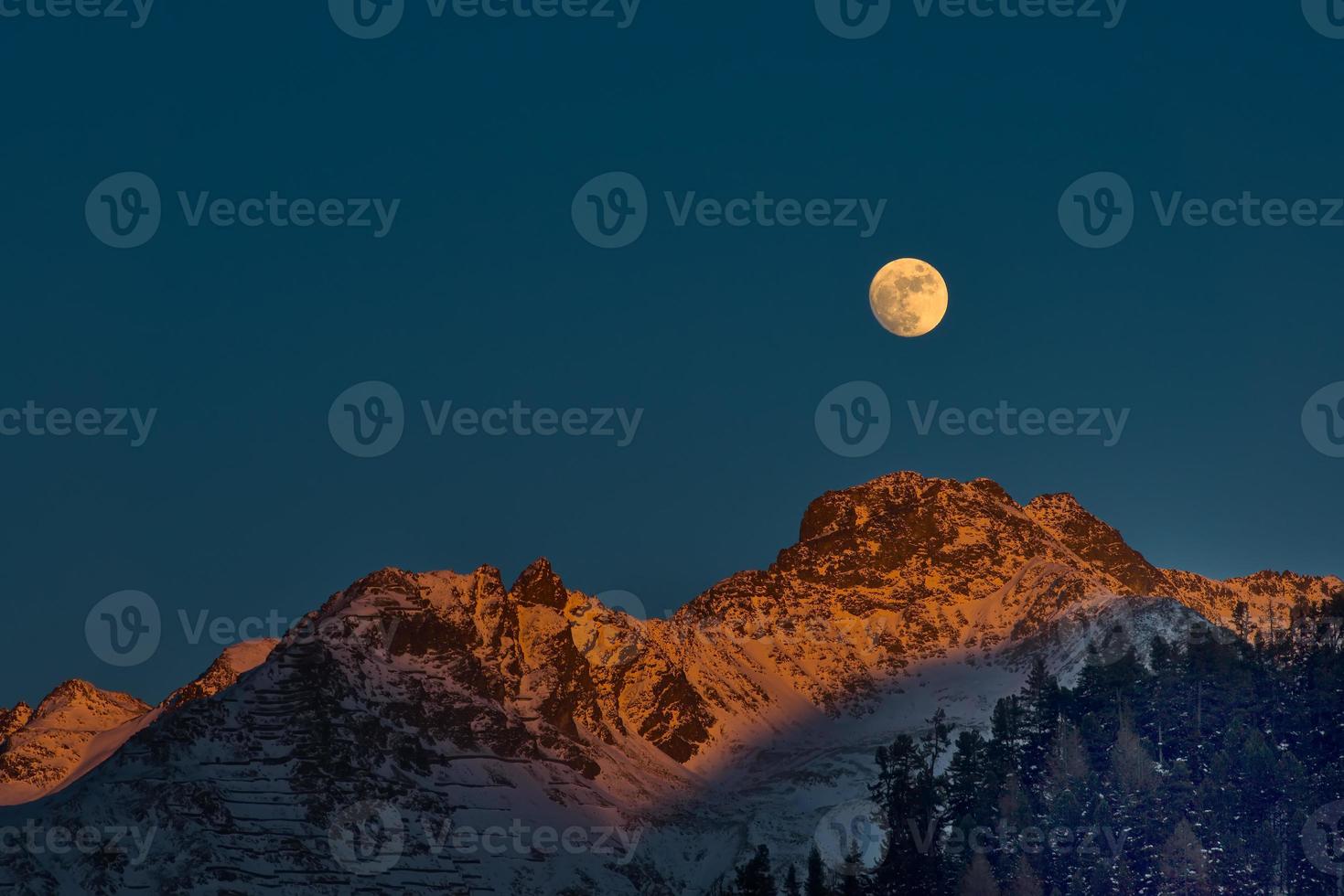 luna llena al atardecer en las montañas de invierno foto