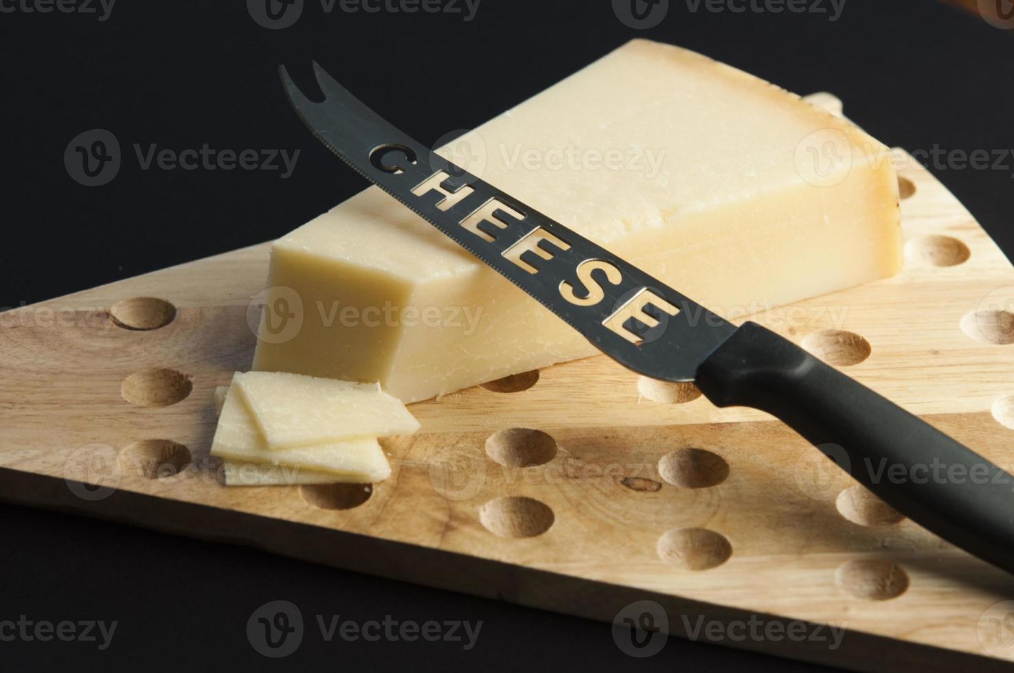 Cheese on a wood cutting table with a special knife for cheese and some slices photo