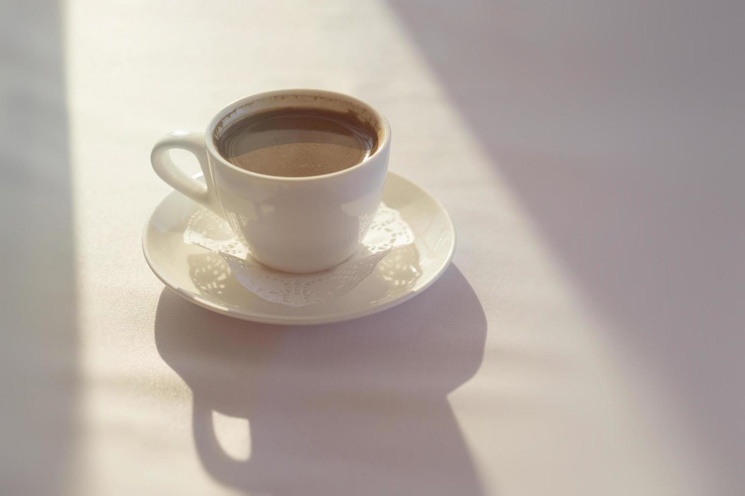 Taza blanca con café turco negro sobre un mantel blanco foto