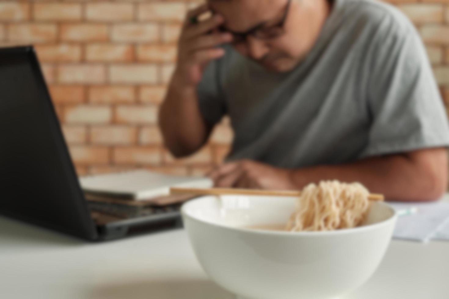 desenfoque de disparo de enfoque, trabajador tailandés ocupado trabajando con una computadora portátil, use palillos para comer fideos instantáneos durante las pausas para el almuerzo en la oficina, porque es rápido y sabroso. con el tiempo comida rápida asiática, estilo de vida poco saludable. foto