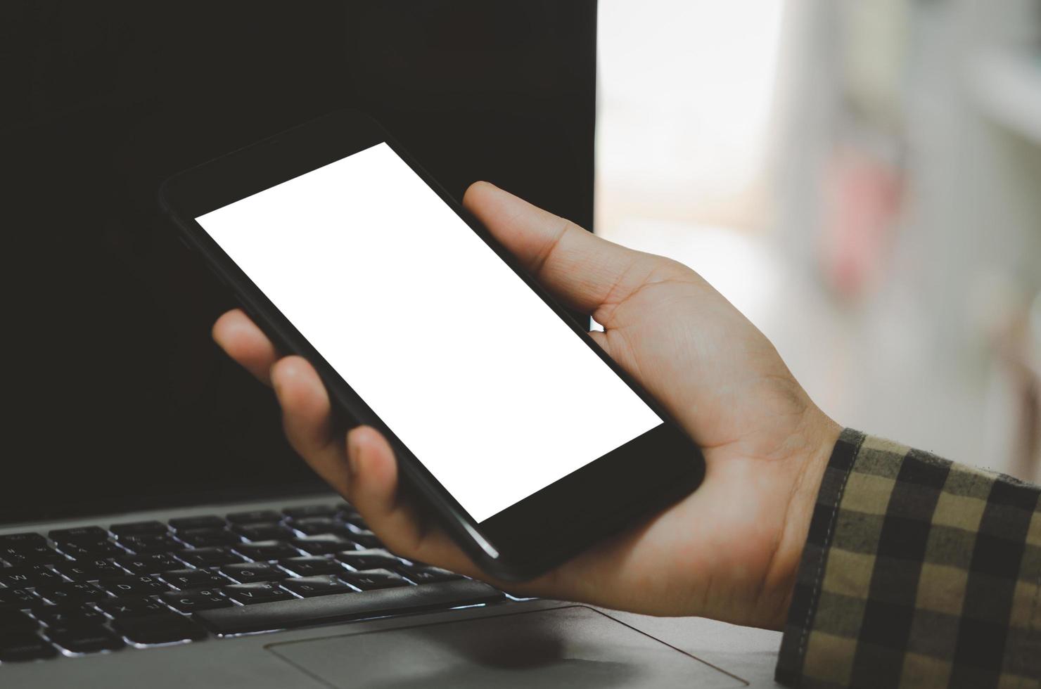 hand holding phone mockup image blank screen computer laptop for advertising text in workplace desk at office. photo