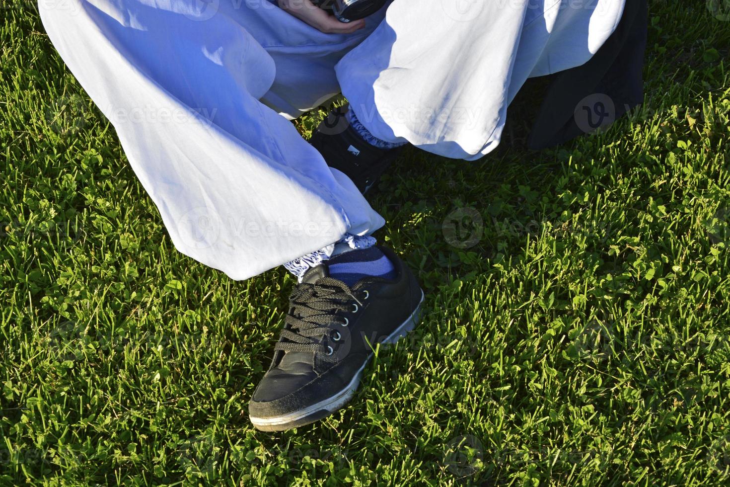 Legs of a teenage girl in blue jeans. The girl is sitting on the grass on the football field. photo