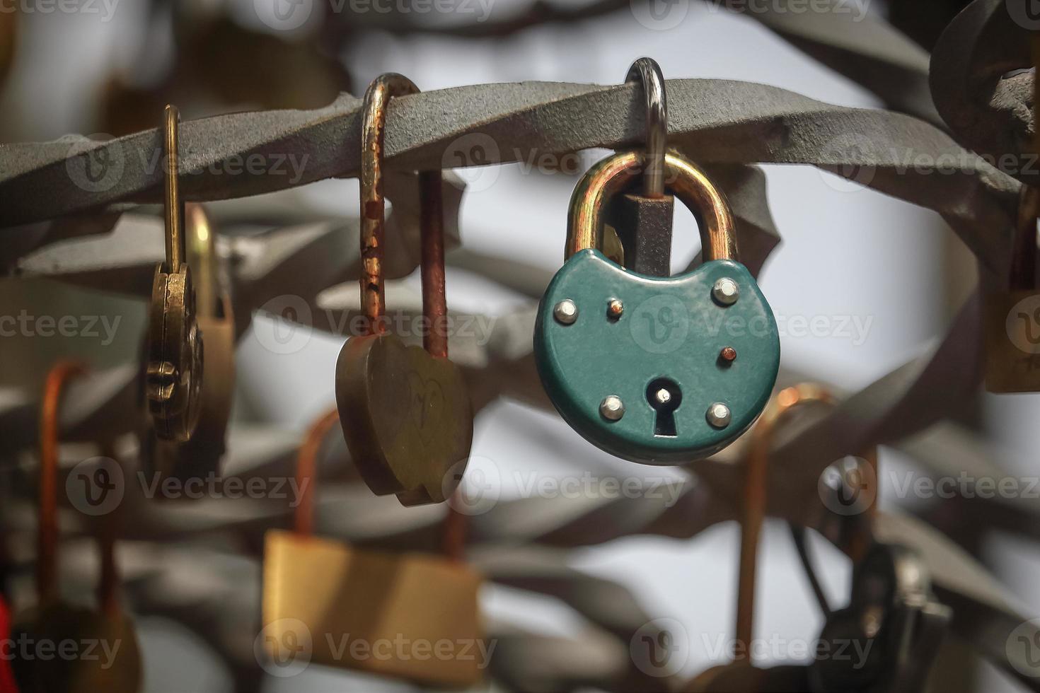 Green padlock hanging on crooked iron bar with many small padlocks photo