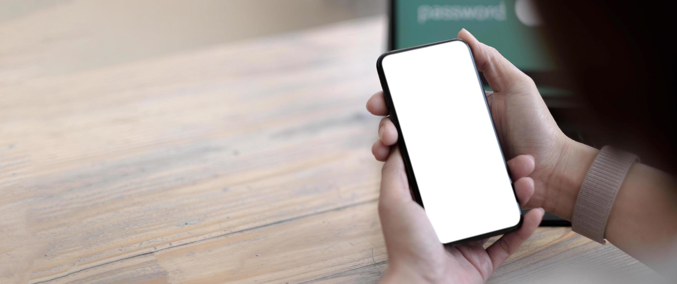 Imagen de maqueta en blanco teléfono celular con pantalla blanca. Mano de mujer sosteniendo mensajes de texto usando el móvil en el escritorio en la oficina en casa. foto