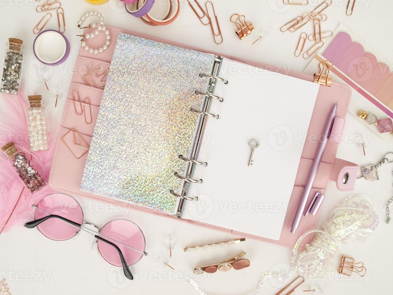 Silver key on the white page of the planner. Diary open with white and holographic page. Top view of the pink planner with stationery. Pink glamour planner decoration photo