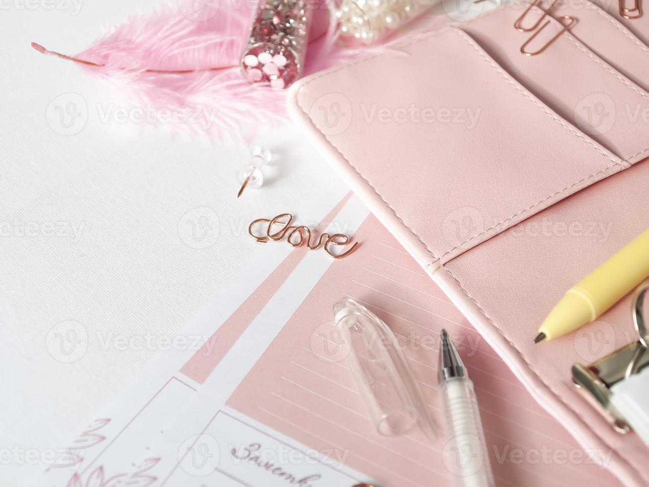 Papelería planificador de oro rosa. amor de letras en forma de alfiler. Lápiz blanco y planificador rosa sobre fondo blanco. foto