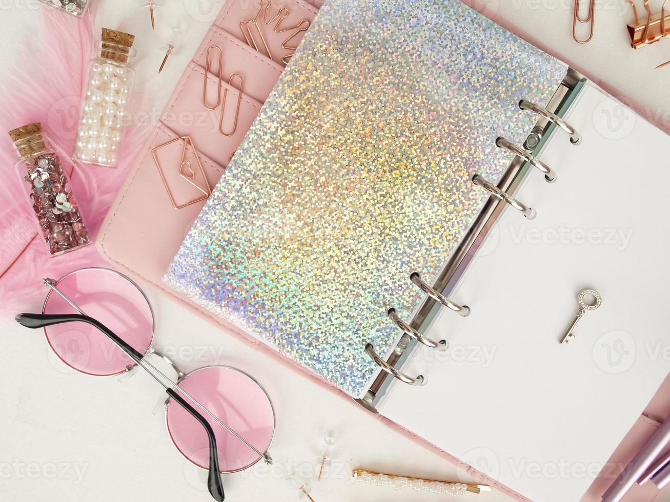 Silver key on the white page of the planner. Diary open with white and holographic page. Pink planner with cute stationery. Top view of the pink planner with stationery. photo