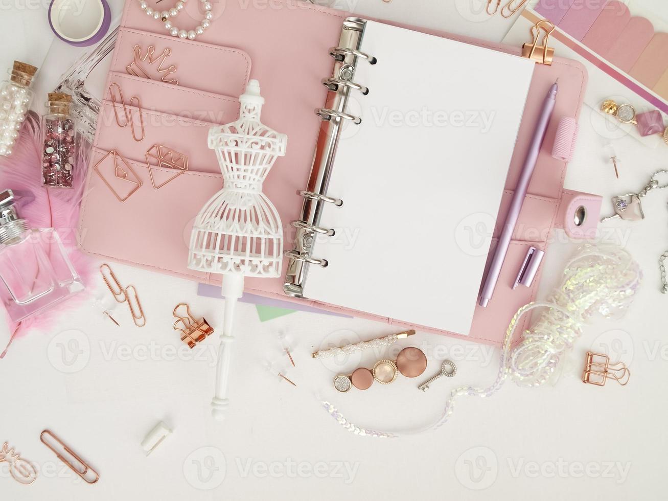 Top view of a pink planner with cute stationery. Pink glamour planner with a white mannequin figurine. Planner with open pages on a white background and with beautiful accessories pens, buttons, pins. photo