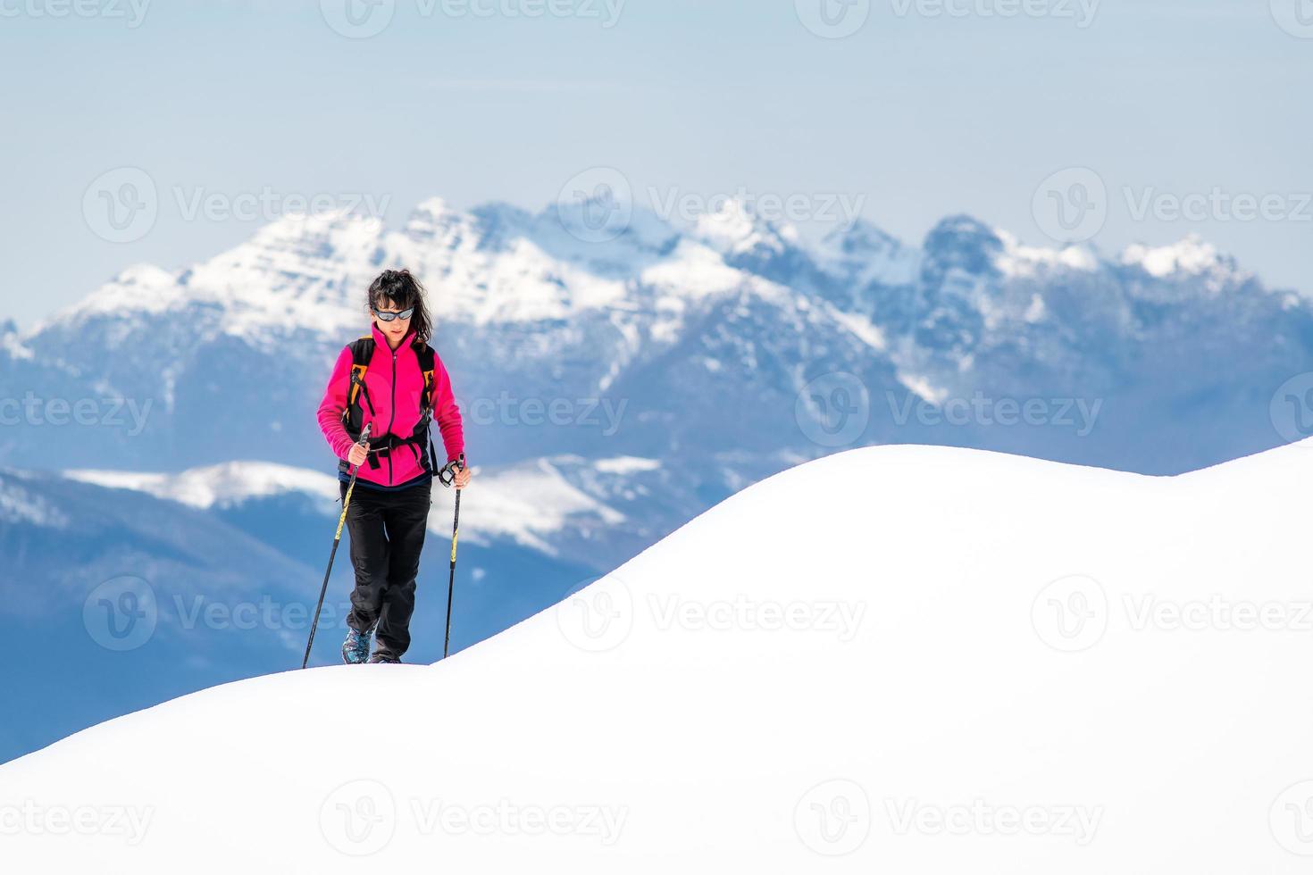 Mujer joven en la cresta de tanta nieve se eleva hacia la cima de las montañas foto