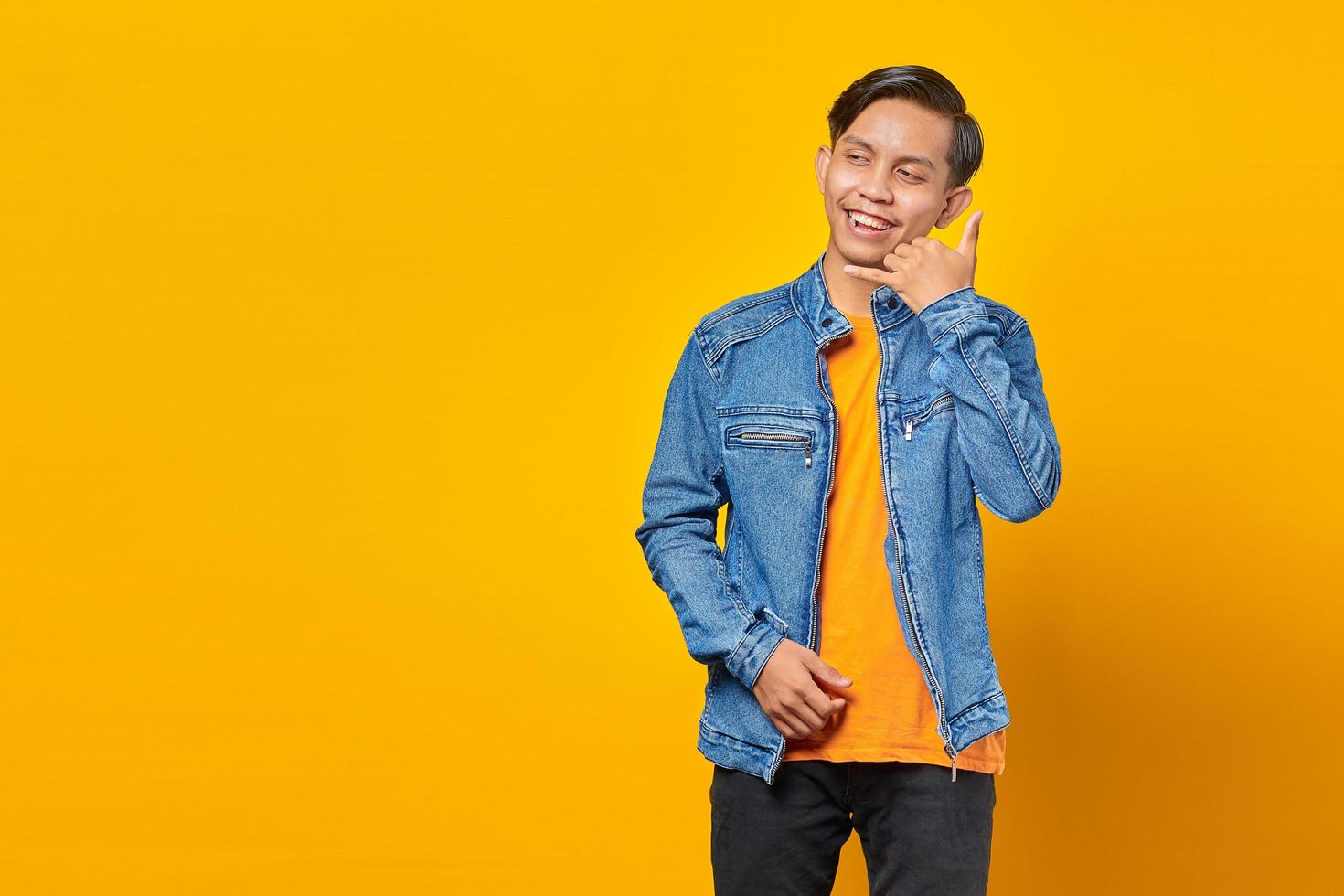 Atractivo hombre asiático haciendo distintivo de llamada y mirando hacia los lados sobre fondo amarillo foto