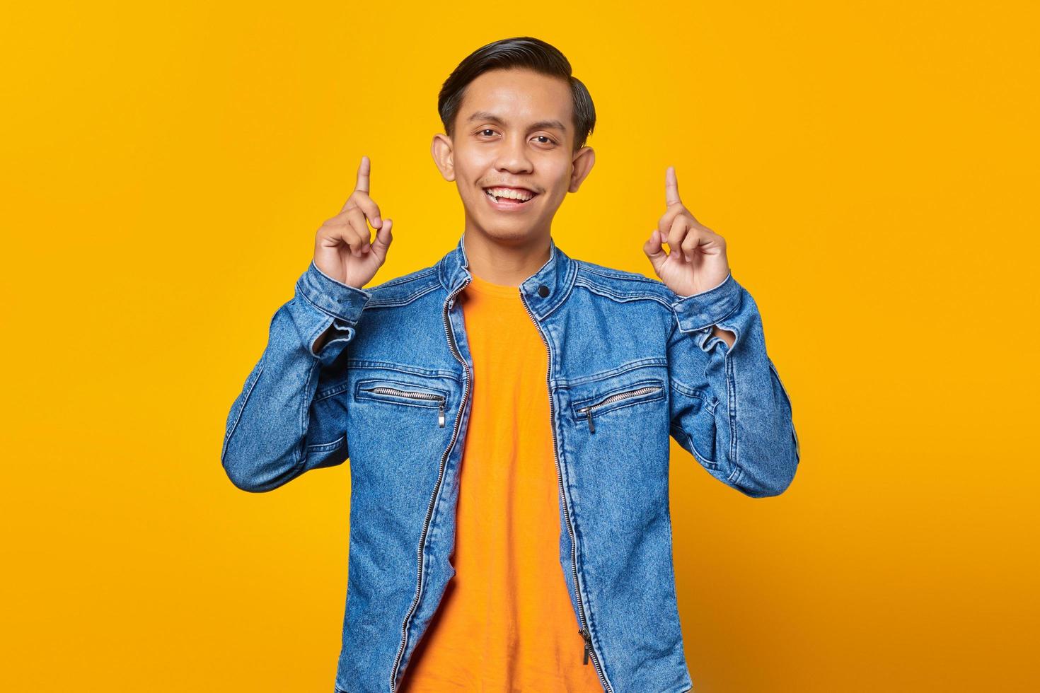 Portrait of cheerful young Asian man pointing at live advertising promotion isolated on yellow background photo